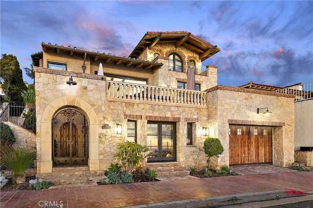 mediterranean / spanish-style home featuring stone siding, decorative driveway, an attached garage, and a balcony