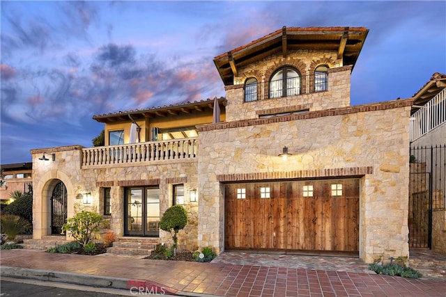 mediterranean / spanish-style house featuring stone siding, decorative driveway, and a balcony