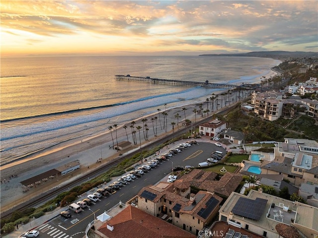 aerial view at dusk featuring a water view and a view of the beach