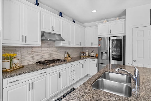 kitchen featuring appliances with stainless steel finishes, white cabinetry, a sink, dark stone counters, and under cabinet range hood