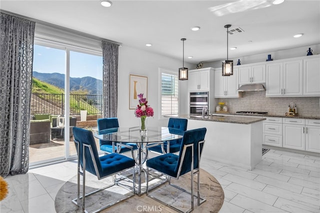 kitchen with white cabinets, marble finish floor, under cabinet range hood, a mountain view, and pendant lighting