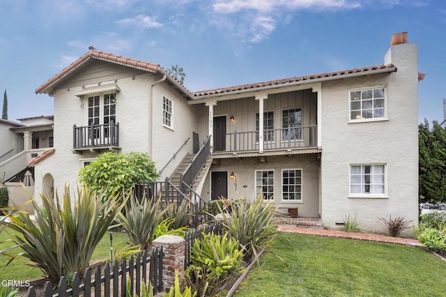 view of front of house featuring a balcony, fence, stairway, stucco siding, and a front yard