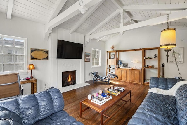 living area with vaulted ceiling with beams, a warm lit fireplace, and wood finished floors