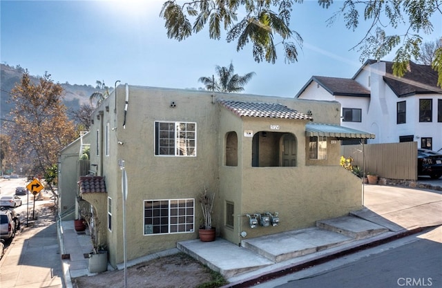 view of front facade featuring fence, a tiled roof, and stucco siding