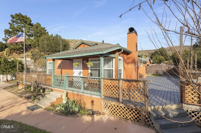 view of front of house with covered porch, a chimney, and fence