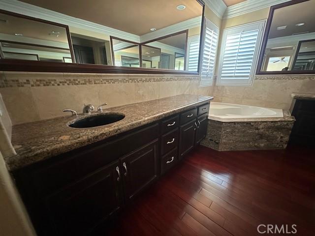 full bath with hardwood / wood-style flooring, a garden tub, crown molding, vanity, and tile walls