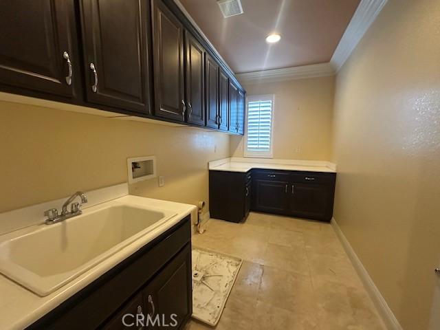 washroom with cabinet space, baseboards, hookup for a washing machine, crown molding, and a sink