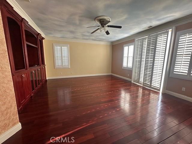 empty room featuring baseboards, ornamental molding, dark wood-style flooring, and a healthy amount of sunlight