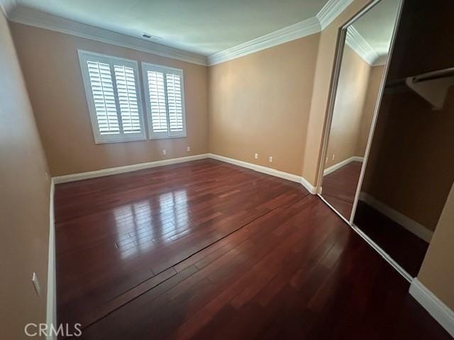 unfurnished bedroom with baseboards, a closet, wood finished floors, and crown molding