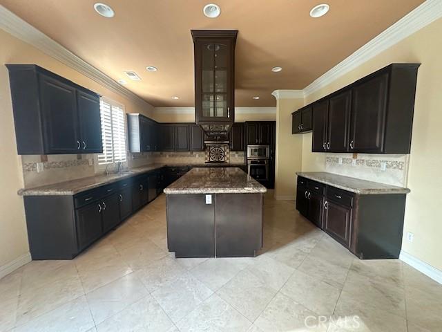 kitchen featuring a center island, stainless steel microwave, wall oven, ornamental molding, and baseboards