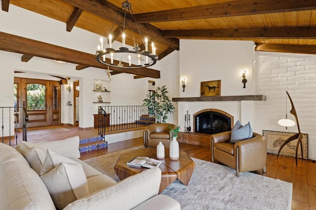 living room with vaulted ceiling with beams, a notable chandelier, a tiled fireplace, wood finished floors, and wooden ceiling