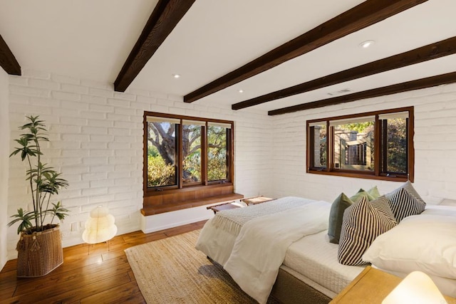 bedroom featuring brick wall, beamed ceiling, and wood finished floors