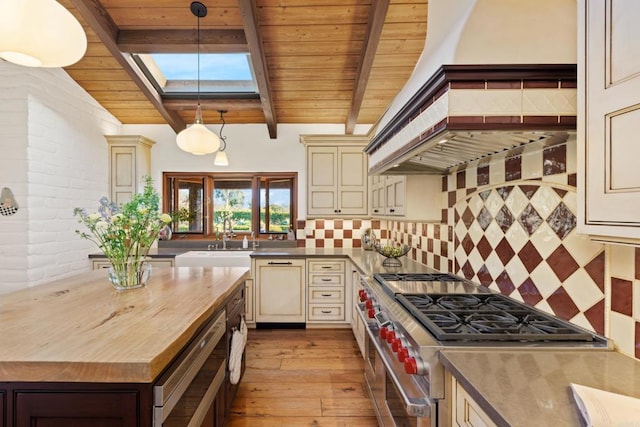 kitchen featuring a sink, cream cabinetry, high end stainless steel range oven, decorative backsplash, and pendant lighting