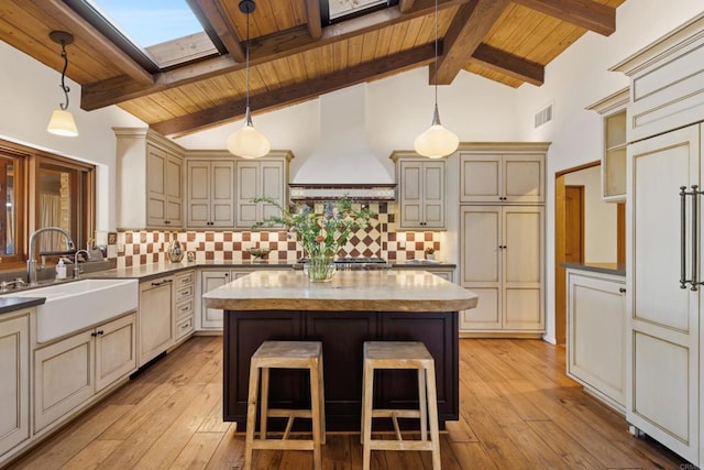 kitchen featuring dishwasher, a center island, cream cabinets, premium range hood, and a sink