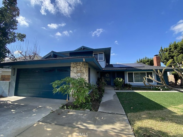 view of front of property featuring solar panels, concrete driveway, stone siding, an attached garage, and a front lawn