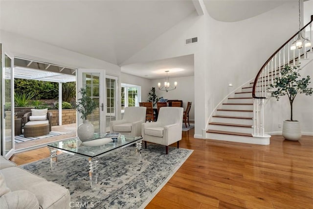 living room with visible vents, stairs, hardwood / wood-style flooring, a notable chandelier, and high vaulted ceiling