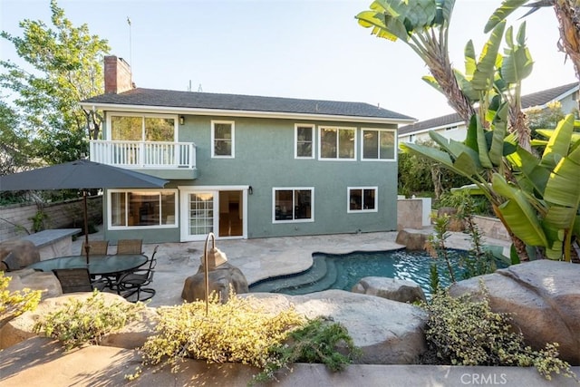 rear view of property featuring fence, stucco siding, a chimney, a balcony, and a patio