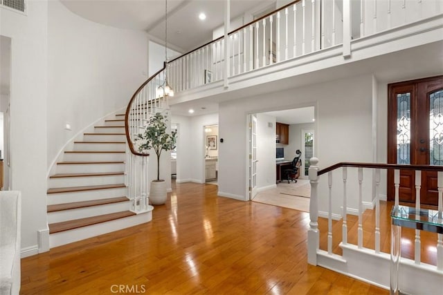 entrance foyer with hardwood / wood-style floors, baseboards, visible vents, french doors, and a towering ceiling