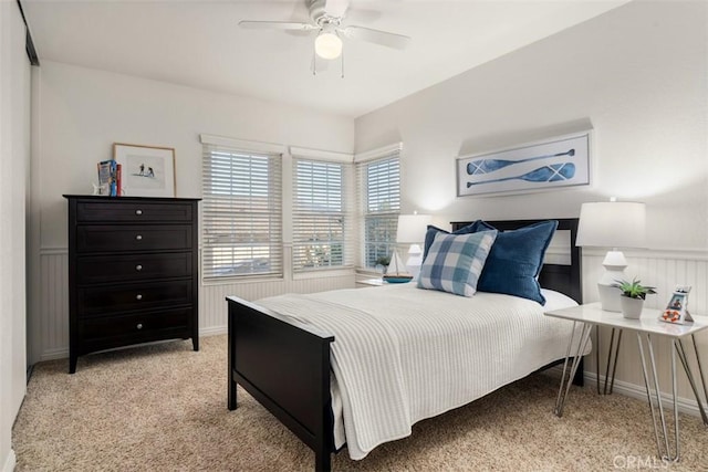 bedroom with a ceiling fan, light colored carpet, and wainscoting