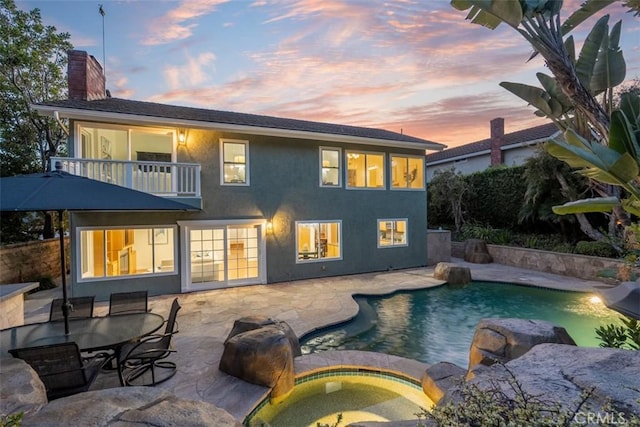 back of house with an outdoor pool, a balcony, an in ground hot tub, a chimney, and a patio area