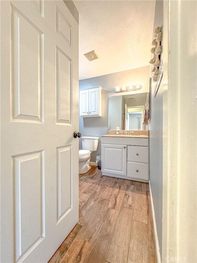 half bath featuring toilet, wood finished floors, vanity, visible vents, and baseboards