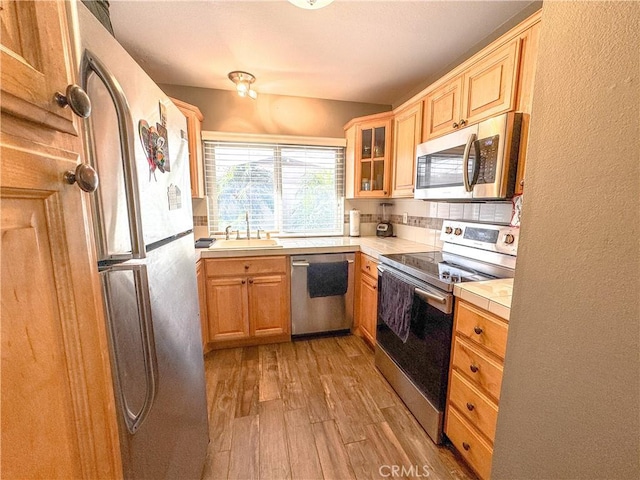 kitchen with stainless steel appliances, tile counters, light wood-style flooring, glass insert cabinets, and a sink