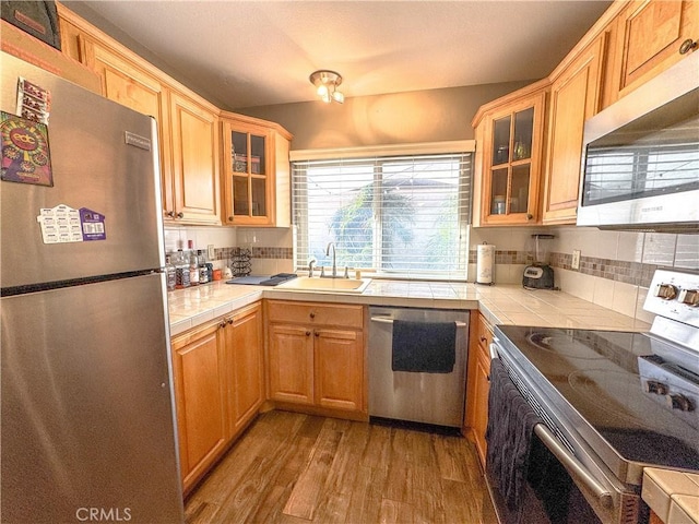 kitchen featuring appliances with stainless steel finishes, glass insert cabinets, tile countertops, and a sink