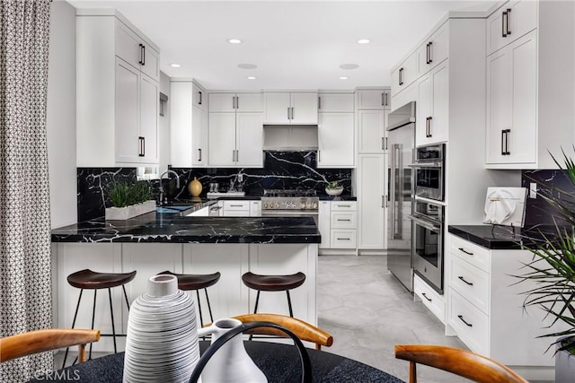 kitchen featuring a peninsula, a sink, white cabinets, a kitchen breakfast bar, and backsplash