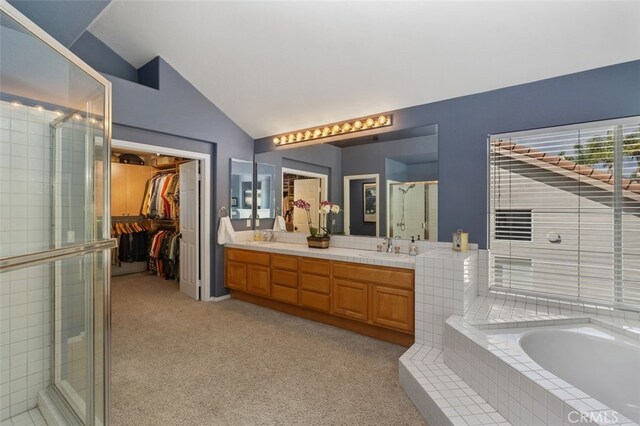 full bath with a walk in closet, a garden tub, a stall shower, vaulted ceiling, and a sink