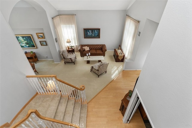 living area featuring arched walkways, stairway, light wood-type flooring, and baseboards