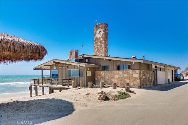 view of front of property with a water view, stone siding, board and batten siding, and a view of the beach