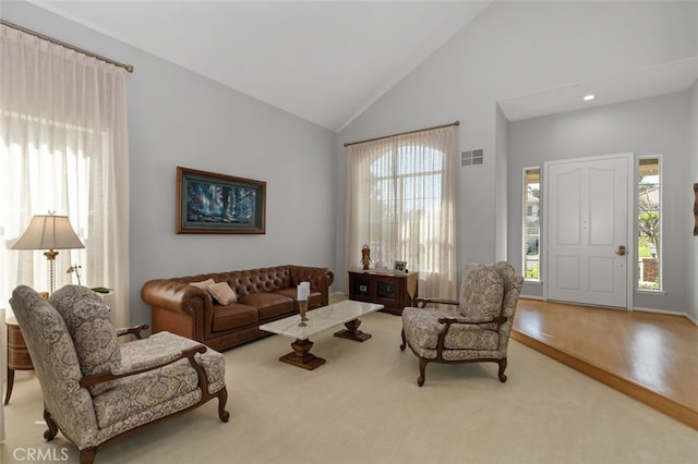 living room with high vaulted ceiling, light wood-type flooring, and visible vents