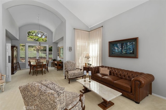 living room featuring high vaulted ceiling, light colored carpet, a notable chandelier, and baseboards