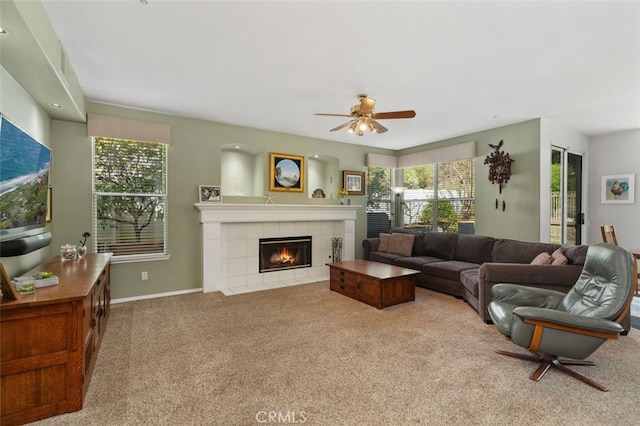 living area with a ceiling fan, a tile fireplace, light carpet, and baseboards