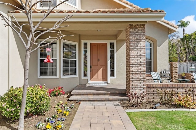 entrance to property with brick siding, a tiled roof, and stucco siding