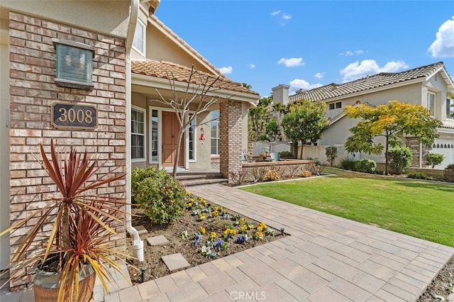 property entrance with brick siding, a lawn, a tile roof, and stucco siding