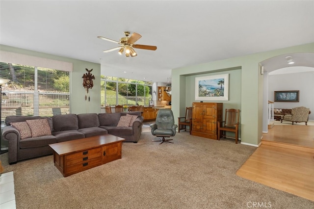 living area with arched walkways, light wood-type flooring, a ceiling fan, and light colored carpet