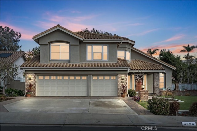 traditional-style home with a garage, brick siding, concrete driveway, a tiled roof, and stucco siding