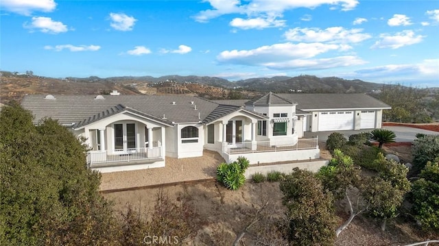 rear view of house with an attached garage, a mountain view, a tile roof, driveway, and french doors