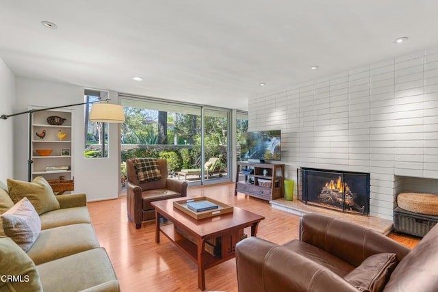 living area with light wood-style floors, recessed lighting, a large fireplace, and expansive windows