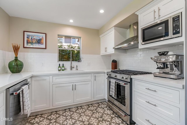 kitchen with stainless steel appliances, a sink, white cabinetry, light countertops, and wall chimney exhaust hood