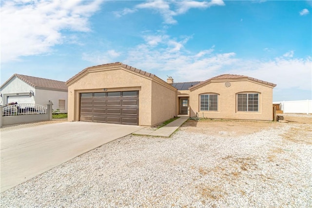 mediterranean / spanish house featuring a garage, concrete driveway, solar panels, and fence