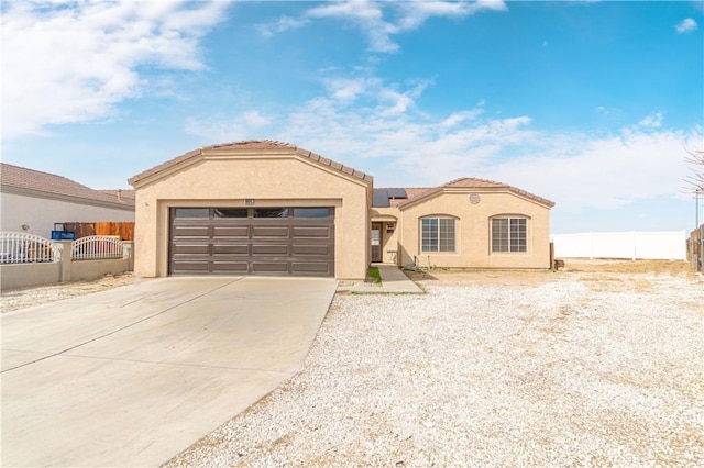 mediterranean / spanish house featuring stucco siding, concrete driveway, an attached garage, roof mounted solar panels, and fence