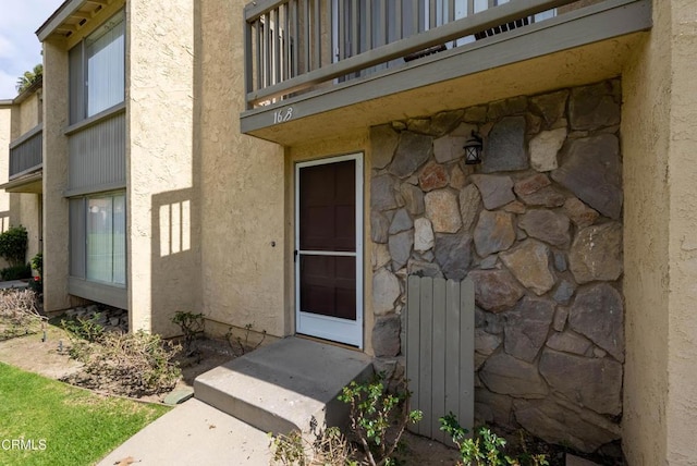 view of exterior entry with stone siding, a balcony, and stucco siding