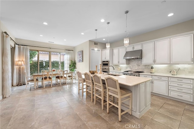 kitchen with white cabinets, an island with sink, decorative light fixtures, light countertops, and under cabinet range hood