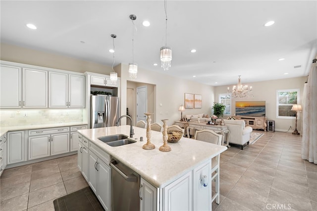 kitchen with decorative light fixtures, a center island with sink, stainless steel appliances, white cabinetry, and a sink