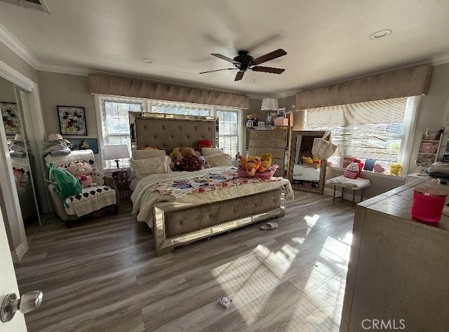 bedroom with ornamental molding, wood finished floors, visible vents, and a ceiling fan