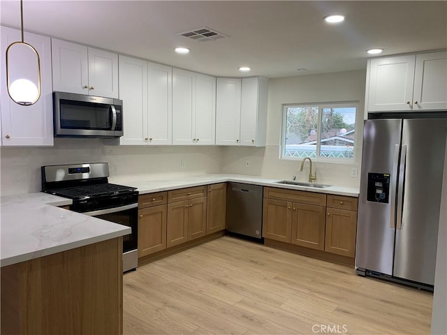 kitchen with appliances with stainless steel finishes, a sink, visible vents, and light wood-style floors