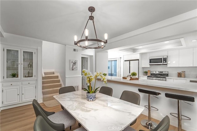 dining area with visible vents, stairs, light wood-type flooring, a tray ceiling, and an inviting chandelier