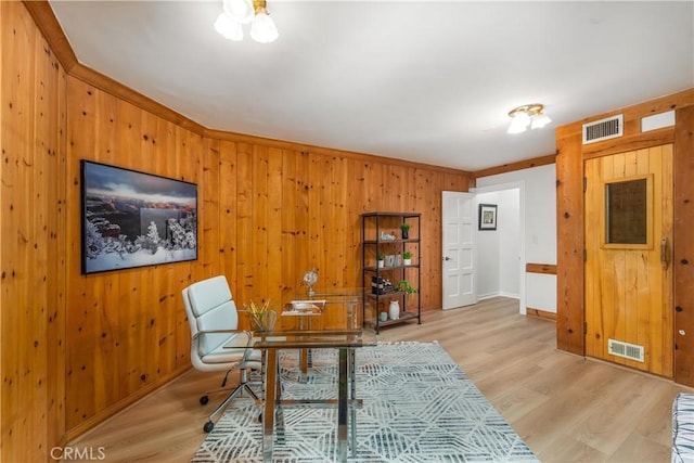 office space with light wood-type flooring, visible vents, wood walls, and baseboards